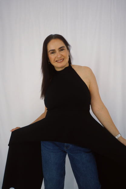 Model wearing a black halter-neck top with an asymmetrical draped hem, holding the flowing fabric to show movement.