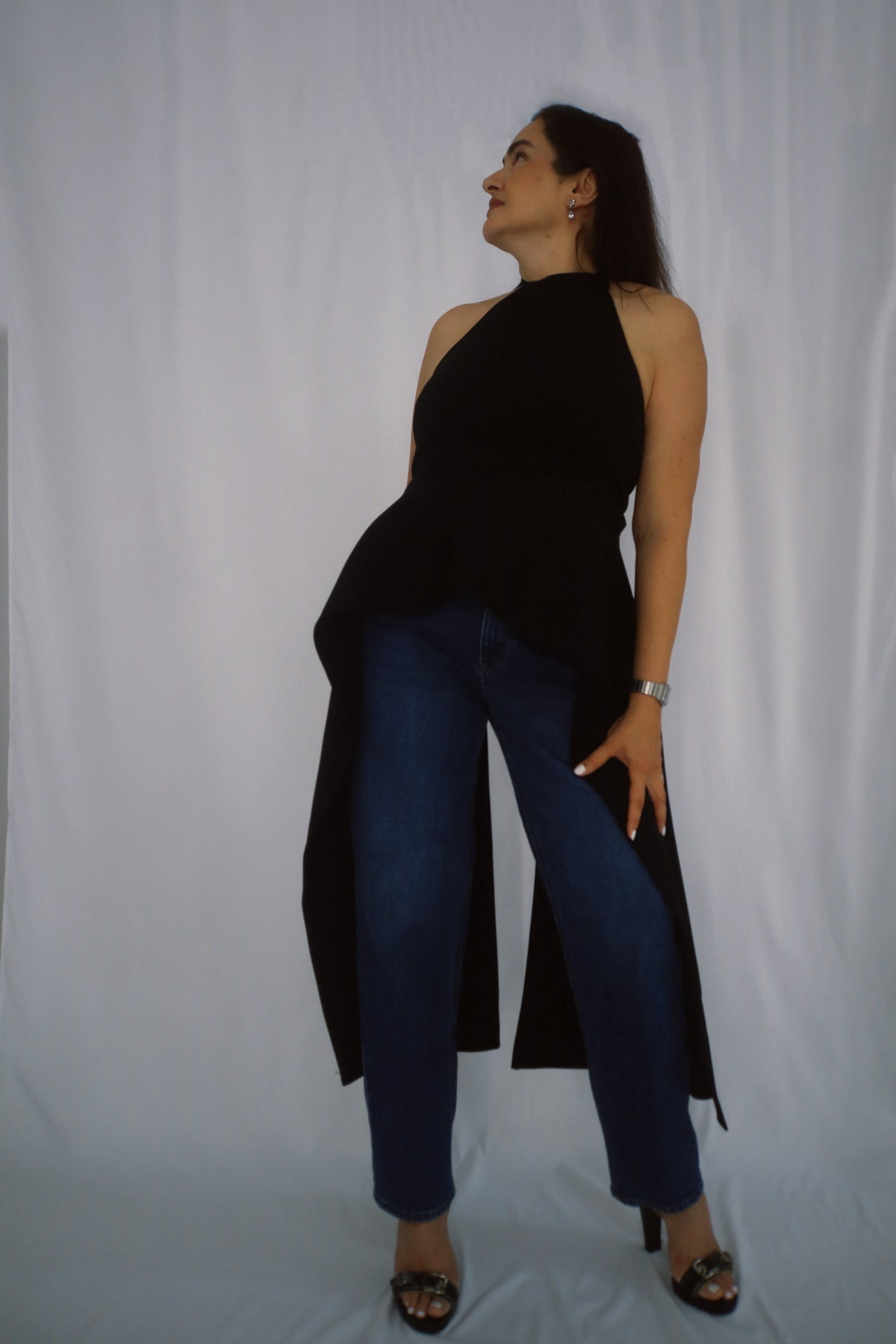 Sleeveless black halter top featuring a dramatic draped hem, paired with denim for a relaxed yet elegant look.