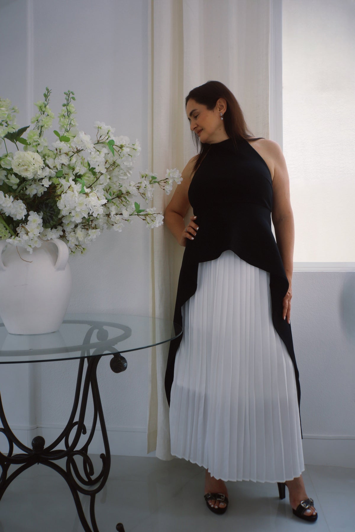 Sleeveless black halter top featuring a high neckline and flowing asymmetrical overlay worn by a model against a neutral background.