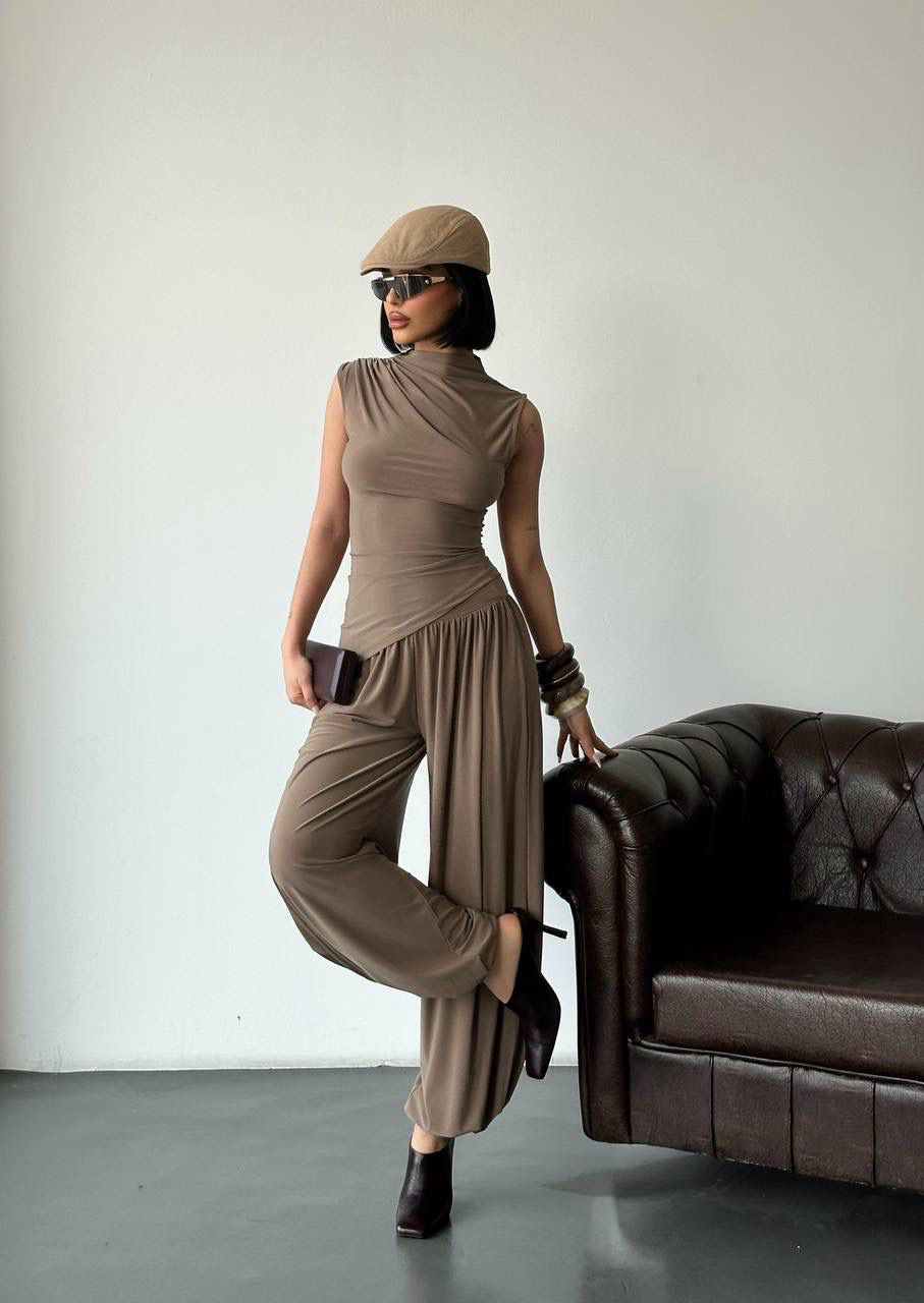 Woman wearing The Sienna Drape Set in black featuring a sleeveless draped top and wide-leg trousers styled with a hat and handbag.