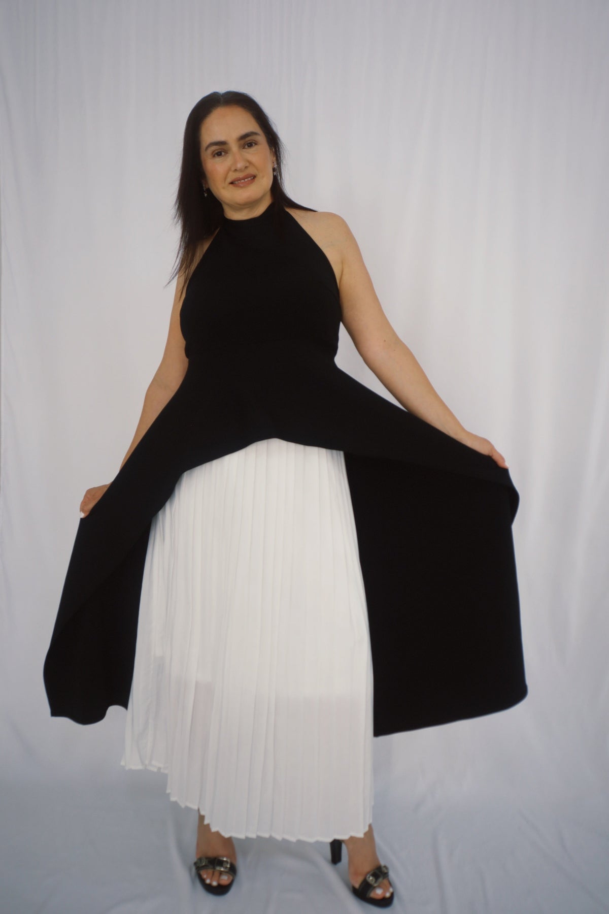 Full-length view of a black halter-neck top with an uneven draped hem paired with a white pleated midi skirt.
