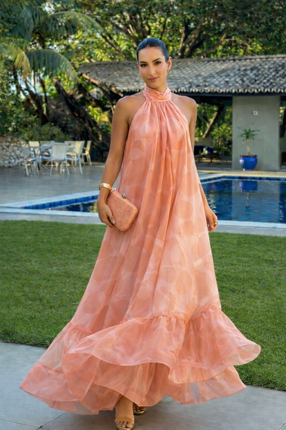 Flowing peach halter maxi dress with a soft silhouette and ruffled hem styled outdoors in a warm-weather setting