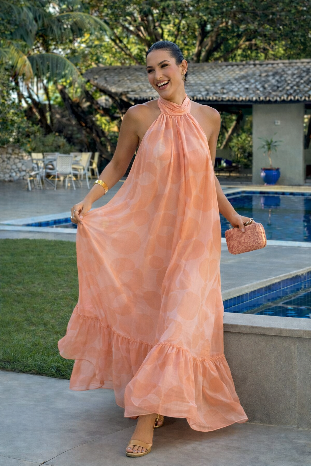 Woman wearing a peach halter neck maxi dress with a flowy silhouette and ruffled hem, styled outdoors near a pool