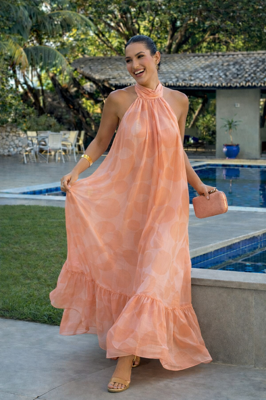 Woman wearing a peach halter neck maxi dress with a flowy silhouette and ruffled hem, styled outdoors near a pool
